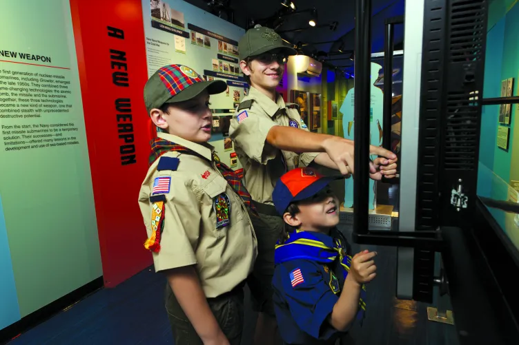 Three Boy Scouts engaging with an exhibit.