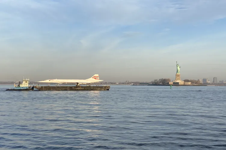 British Airways Concorde jet on a barge in the Hudson River passing by the Statue of Liberty.