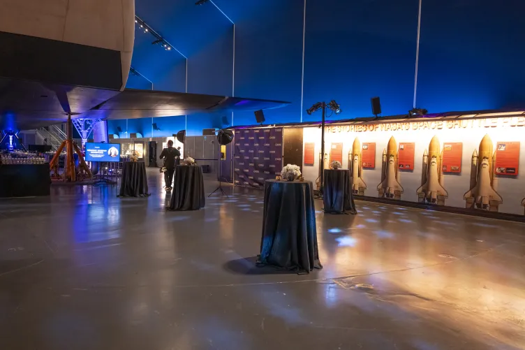 Cocktail reception in the Space Shuttle Pavilion with high top tables and step and repeat banner