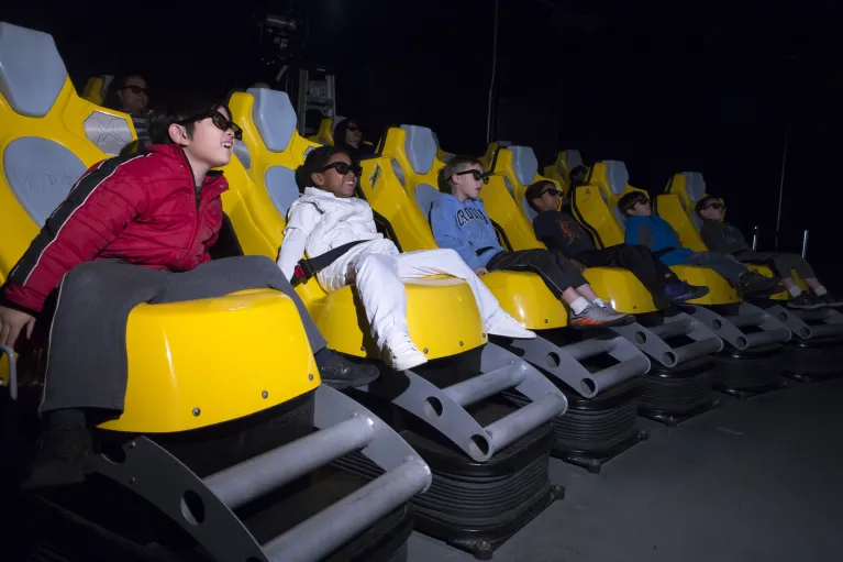 Image of children in 3-D glasses enjoying a ride on the 4-D simulator experience, Stories of Intrepid 
