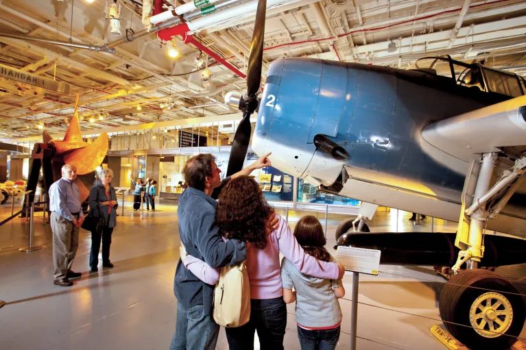 A family looks closely at a blue Avenger aircraft on Intrepid's hangar deck