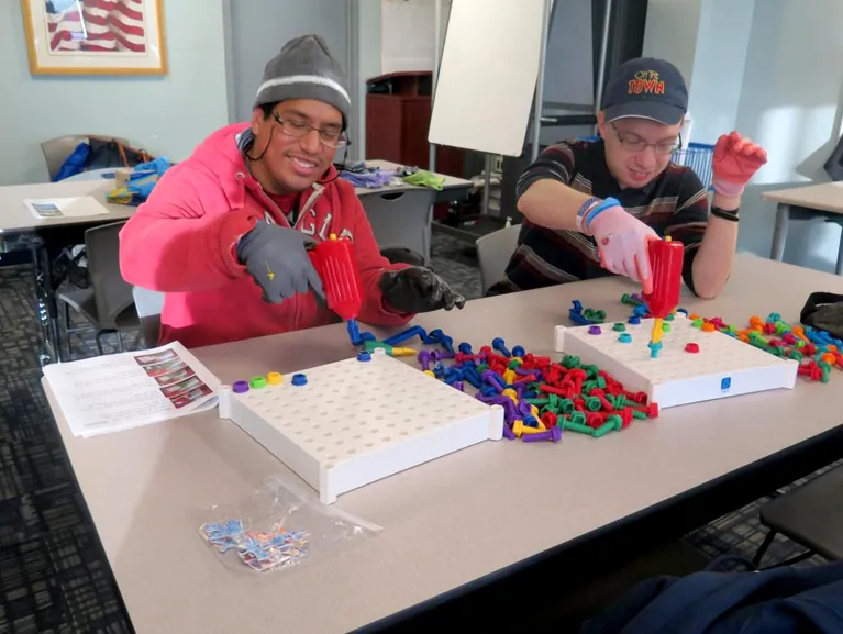 Two students are in a classroom playing with nuts and bolts toys.