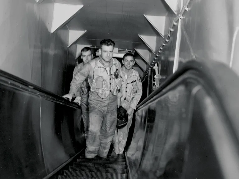 Three pilots standing in the middle of the Intrepid's pilot escalator.