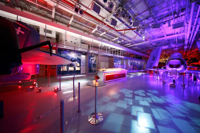 Hangar 2 set for a cocktail reception with a bar, high top table and uplighting on the aircraft in red and white