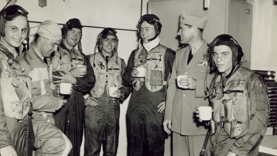 An archival photo of a group of pilots in uniform are having a cup of coffee.