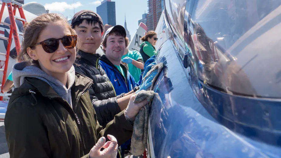A team of corporate volunteers actively washing an aircraft on the Intrepid flight deck.