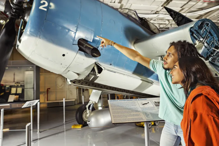Two teenagers stand by a blue Avenger plane on the ship's hangar deck