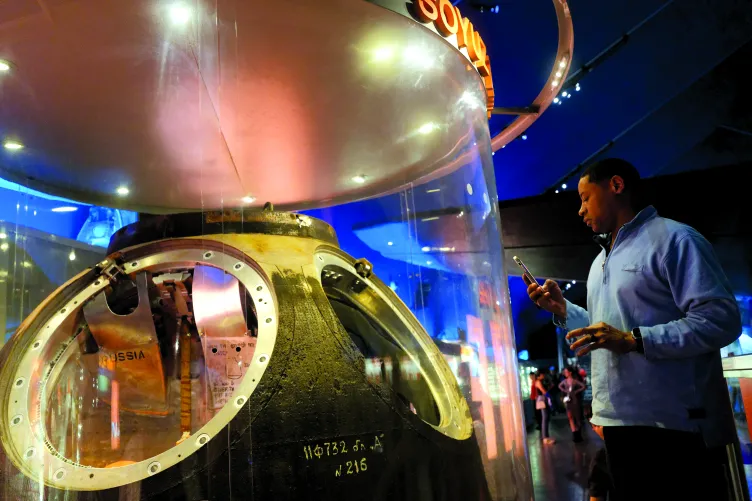 A visitor looking at the interior of the Soyuz TMA-6 and taking a photo on their cell phone.