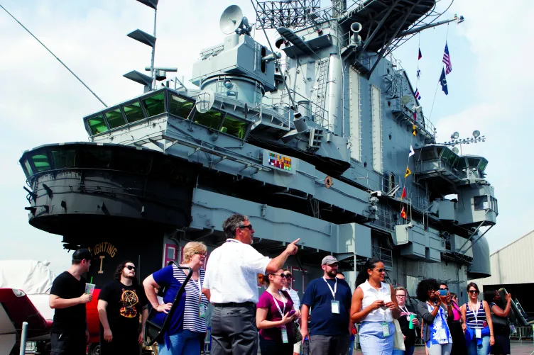 A group of visitors are with a guide on the flight deck with the Island behind them.