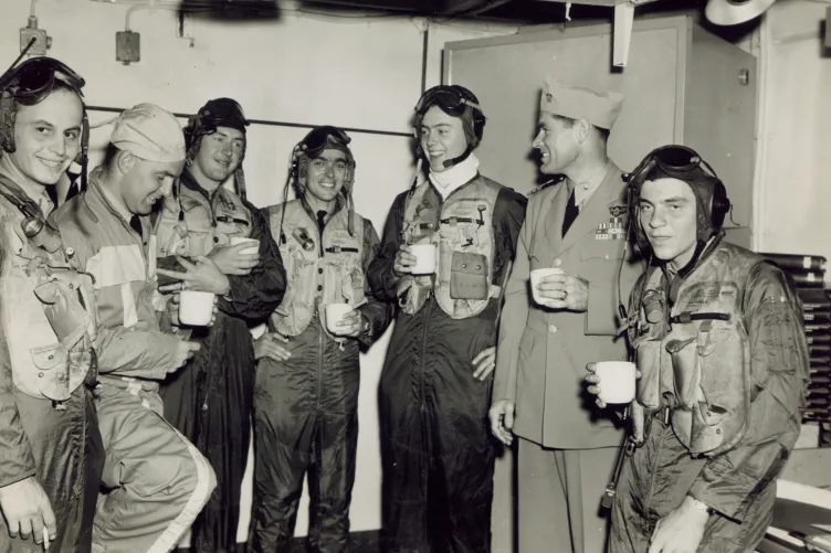 An archival photo of a group of pilots in uniform are having a cup of coffee.