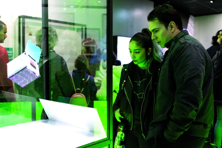 Visitors look at a holographic cube is suspended in mid-air in a display case.