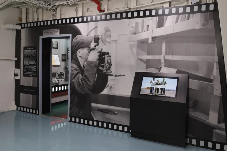 A close up of an exhibition panel designed like a film strip with a video showing excerpts from U.S. Navy training films that show the photographic process.