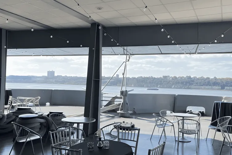 Fantail setup for a cocktail reception with blue linen on tables, decor, and string lighting hanging above.