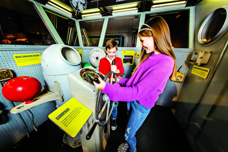 Two children play inside an interactive model of the ship's navigation bridge