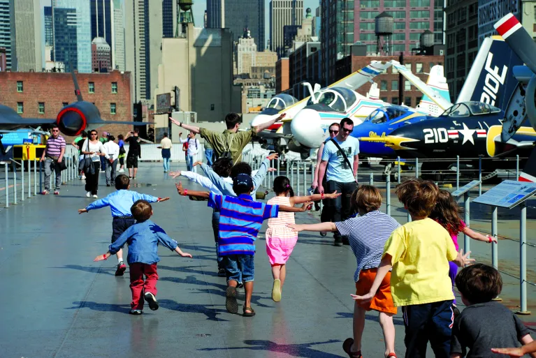 Children on the flight deck with their arms out like they are flying.