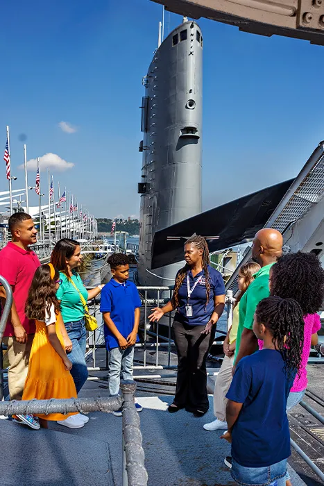 A group of visitors is standing with a Museum educator outside near the Growler.