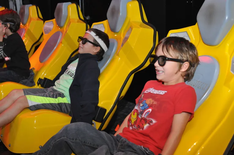 Museum visitors in yellow theater chairs wearing googles in the 4D film