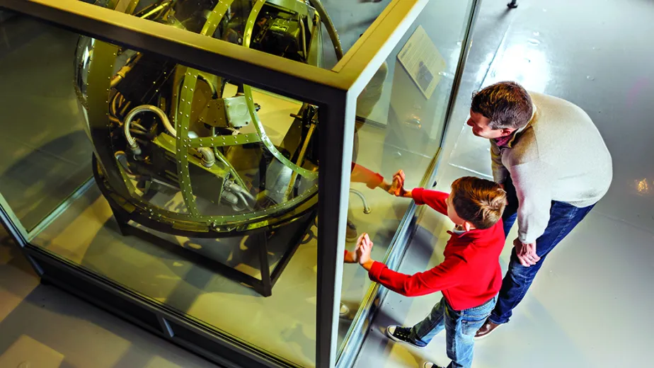 A father and son look with excitement upon a ball turret.