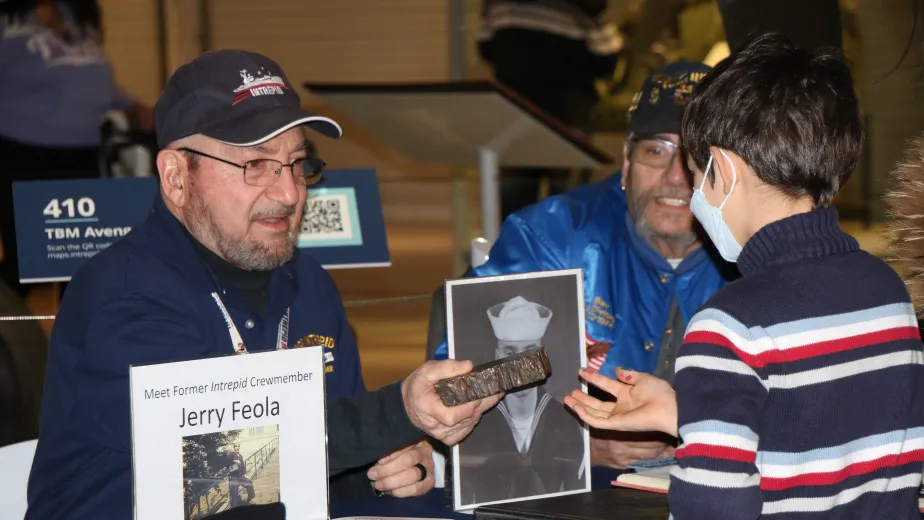 A veteran is seated at a table and showing an artifact to a child.