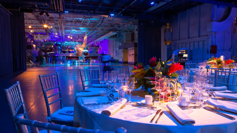 Hangar 2 and Hangar 3 set in blue uplighting, view of Hangar 3 dinner table with florals and overlooking aircraft in Hangar 2